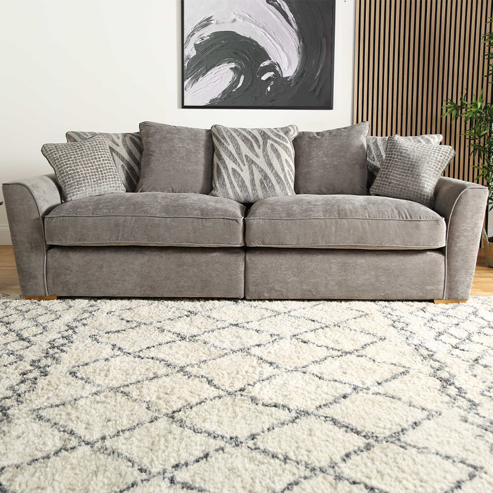 Grey sofa with patterned cushions on a white and grey diamond rug in a living room.