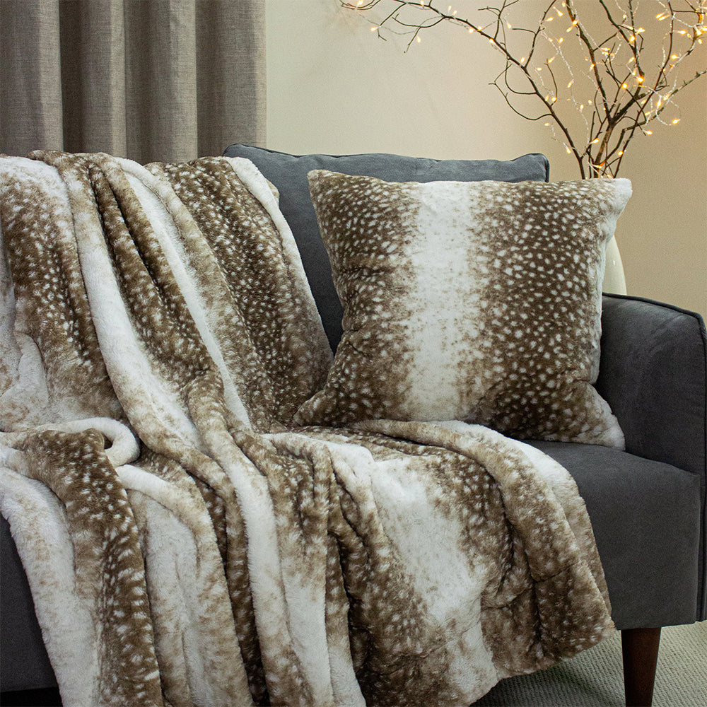 Brown and beige patterned throw blanket and pillow on a gray sofa with decorative lights in the background.