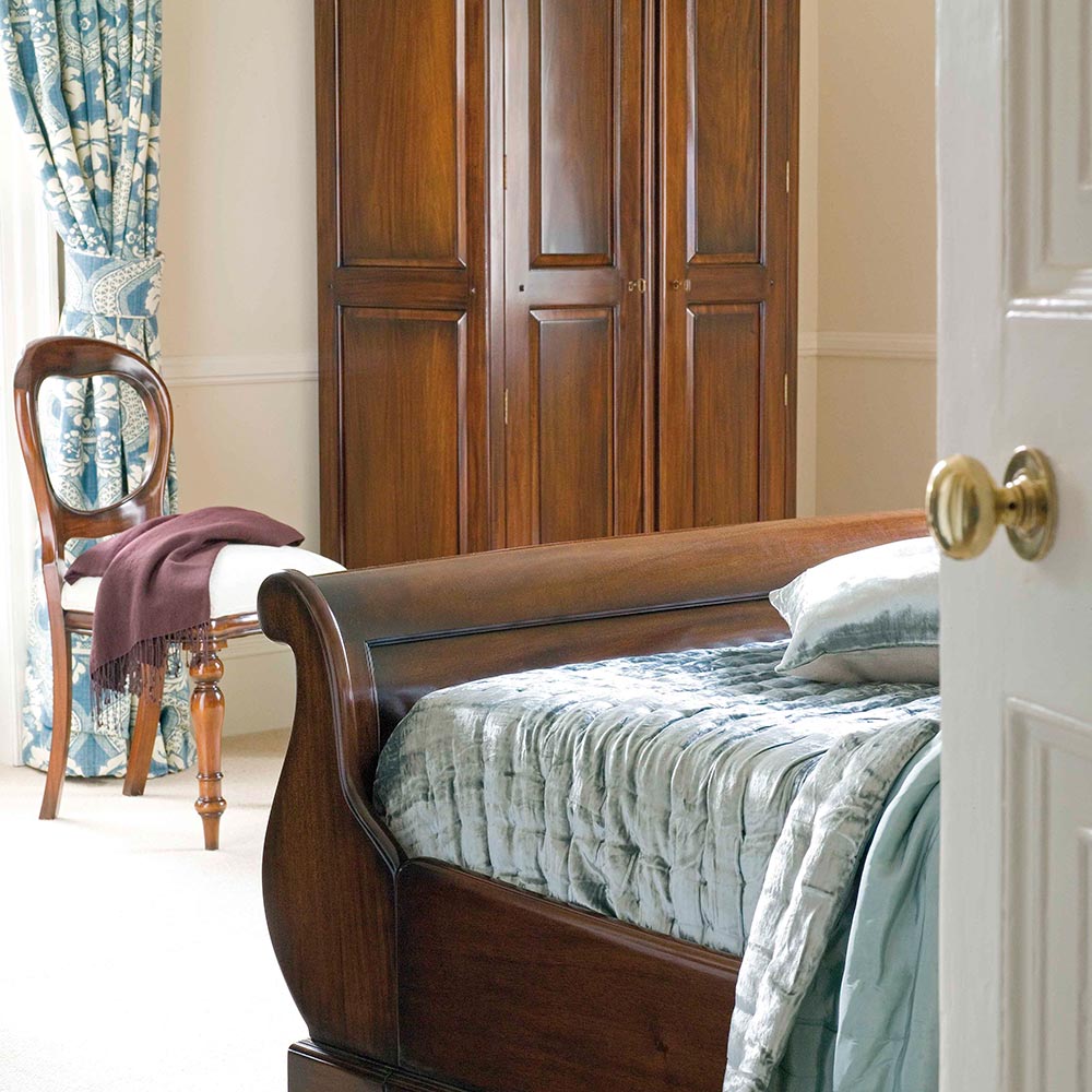 Wooden sleigh bed in a bedroom with a wooden wardrobe and chair.