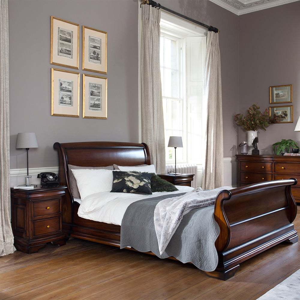 Neatly arranged bedroom with wooden sleigh bed, nightstands, and framed pictures on gray walls.