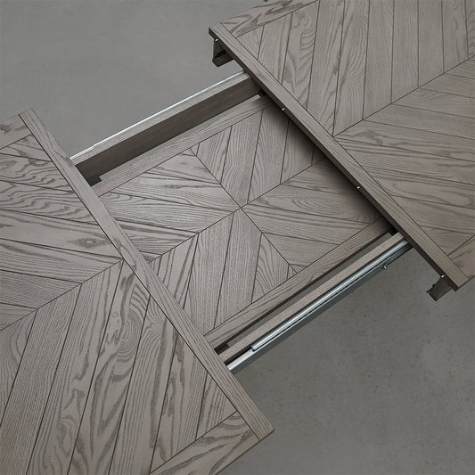 Oval shaped extending wooden dining table with saw-cut ash chevron pattern in silver grey finish