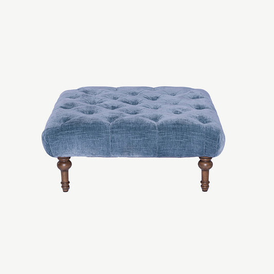 Footstool upholstered in blue fabric with button detailing and wooden legs
