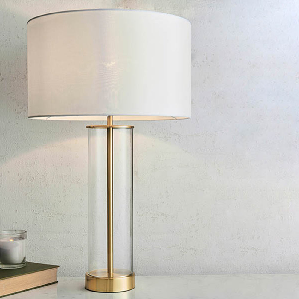 Simple  table light with a clear glass base, vintage white faux silk shade and a brushed gold effect finish